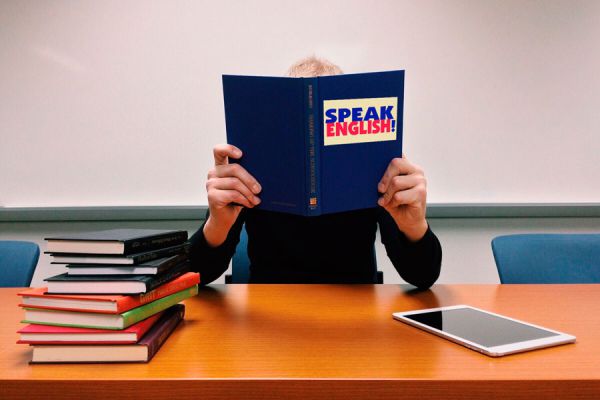 Mujer con libros y tablet estudiando inglés intensivo.